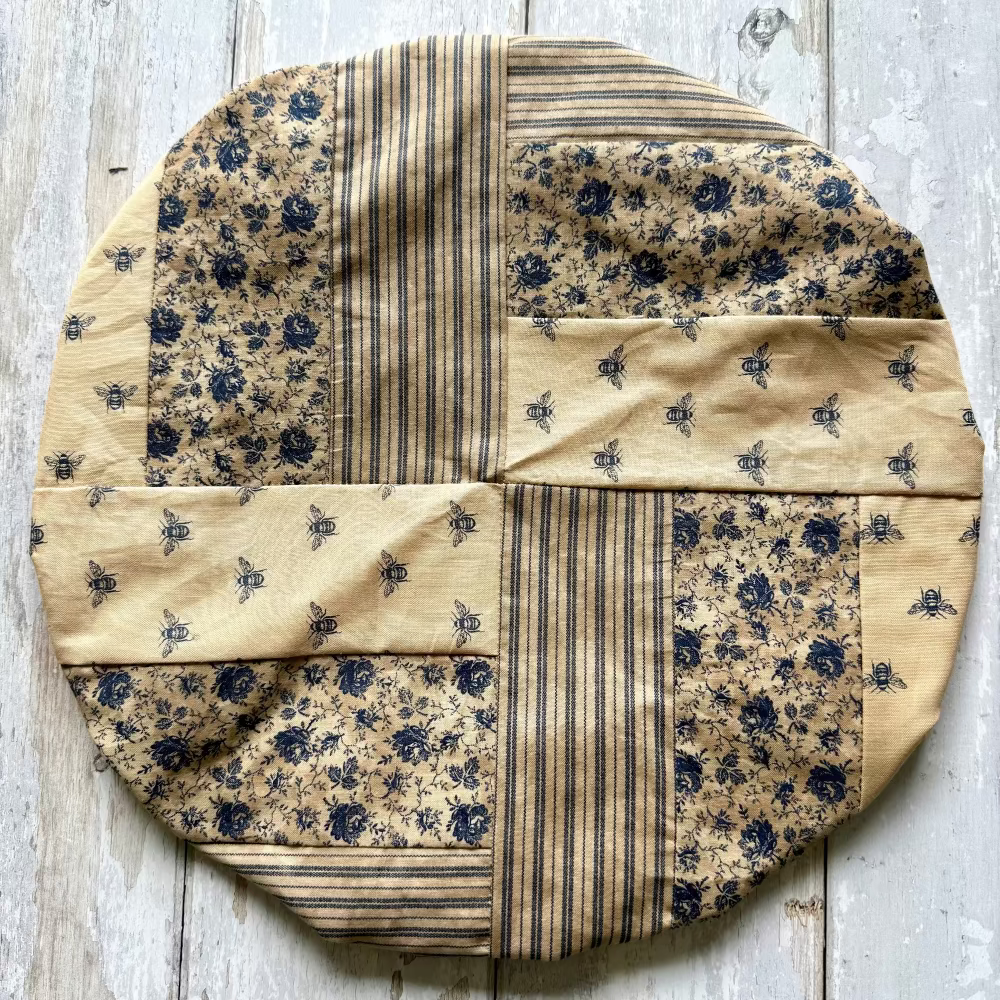 Round patchwork quilt with floral and striped patterns on a wooden surface